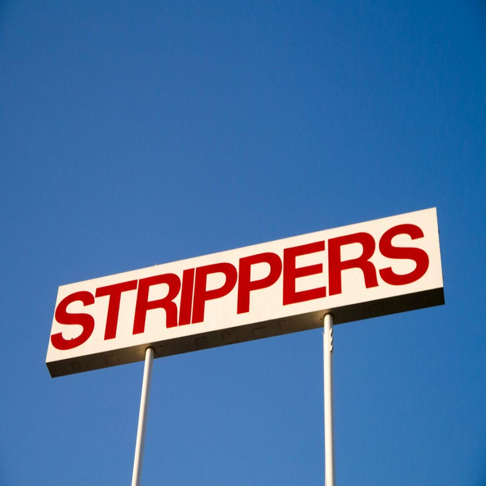 a white tall sign outside of a strip cub with the word “strippers” in red on it